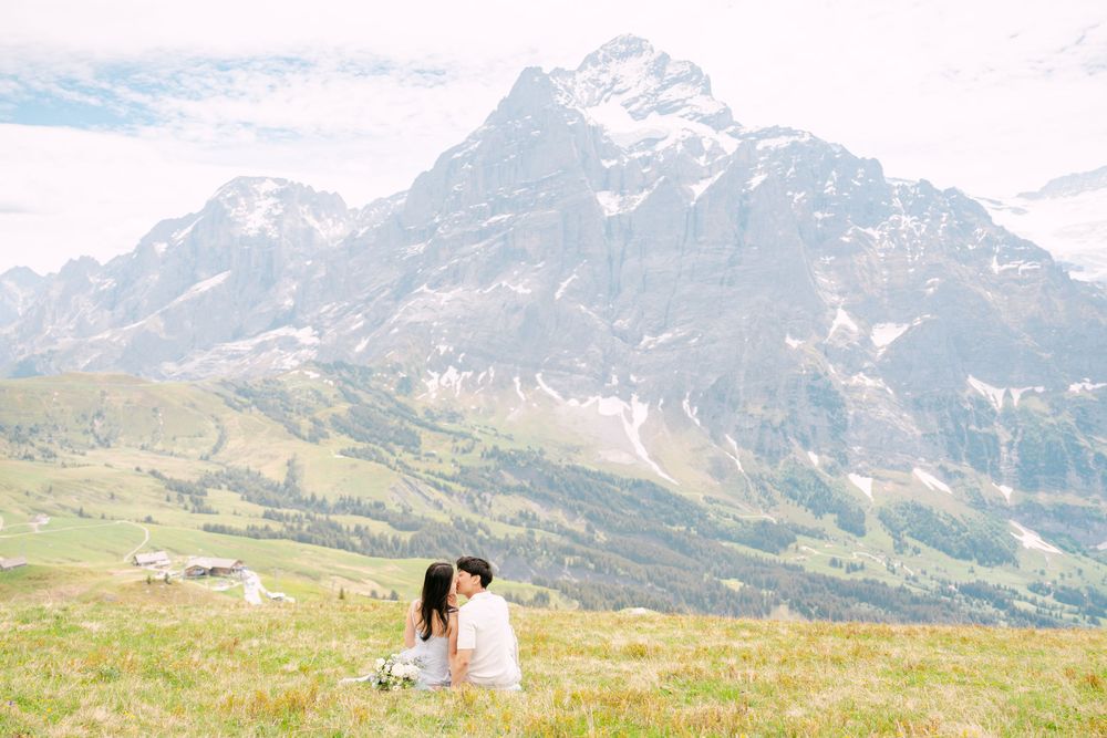 Couple sitting together on alpine meadow with majestic snow-capped mountain peak backdrop in Swiss Alps.