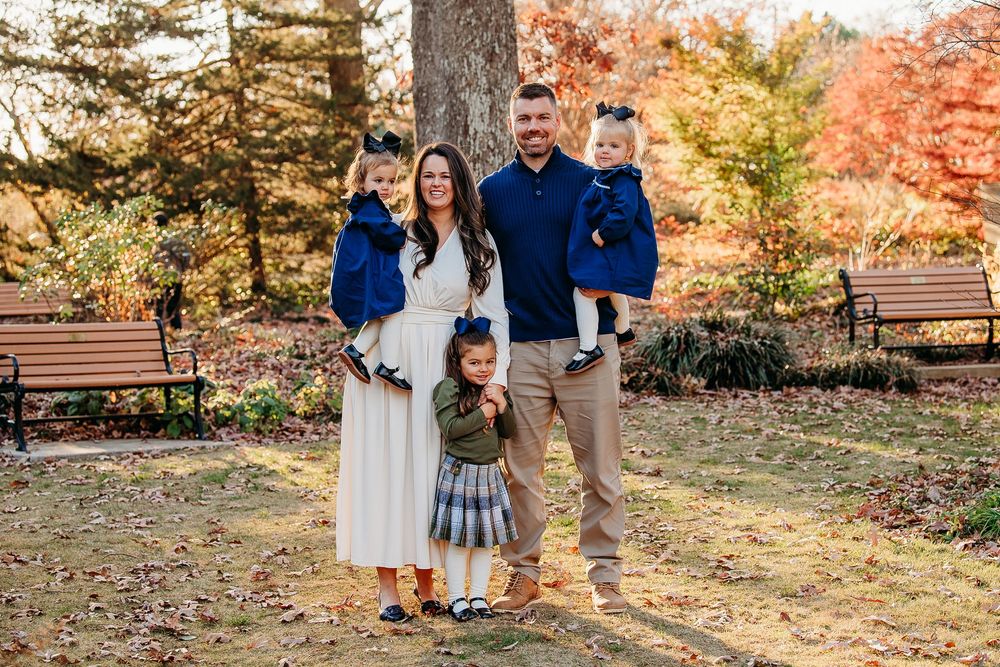 Family of five posing together in a colorful autumn park with fall foliage in background.