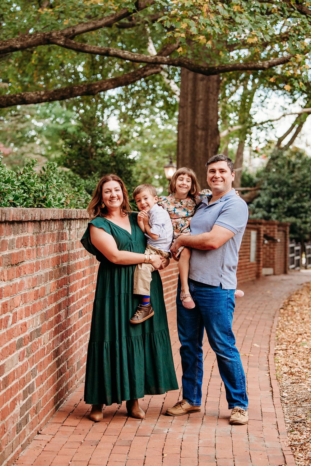 Family of four posing along a brick pathway under a large tree in autumn.