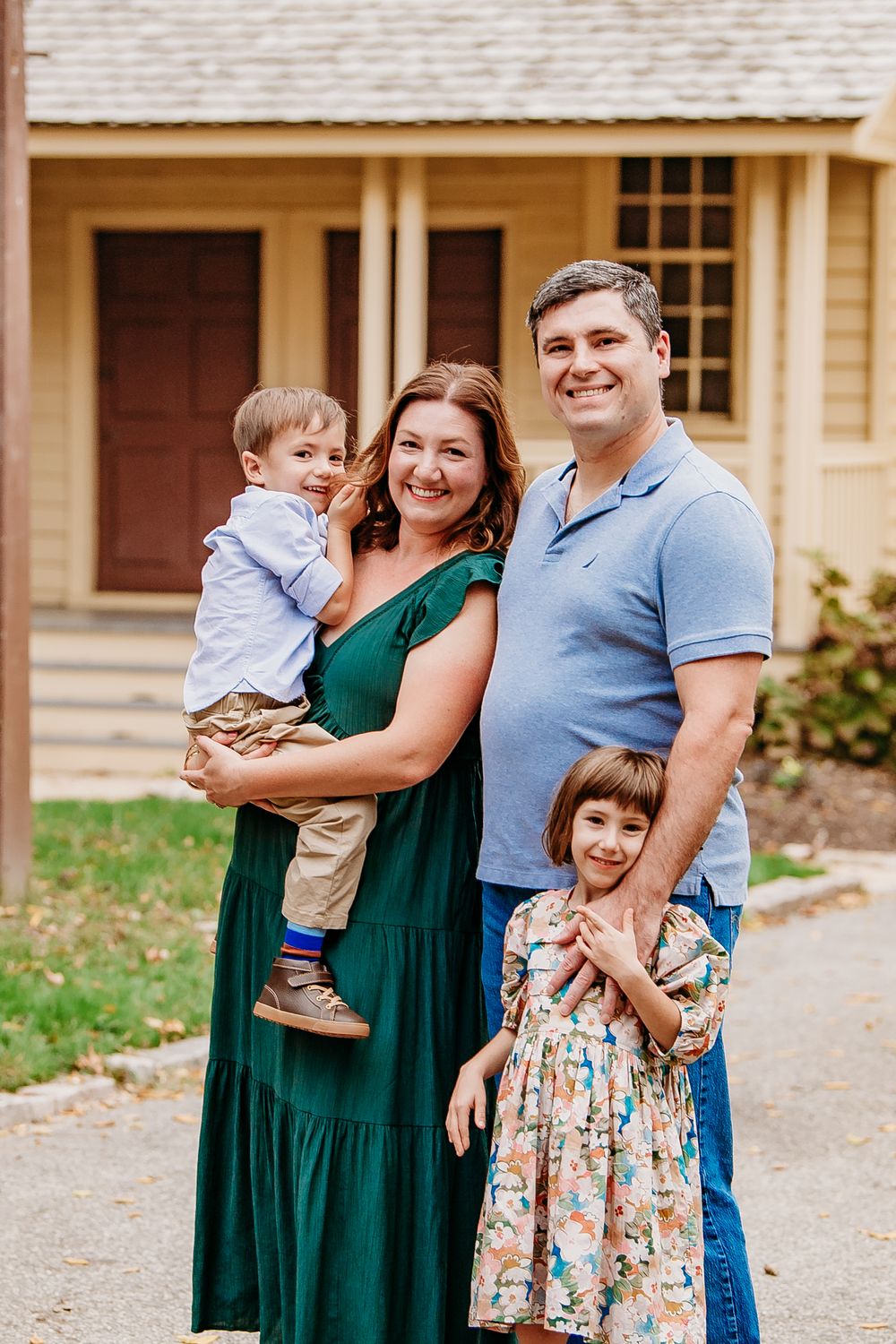 Smiling family of four posing together outdoors in front of a historic yellow building.