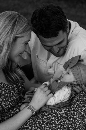 Happy couple smiles at their newborn baby girl lying in mom's lap in black and white portrait.