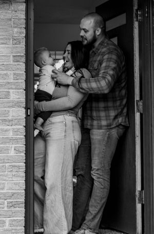 Black and white photo of happy couple with newborn baby standing in a doorway.