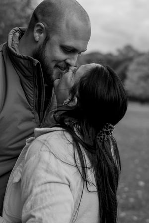 Black and white portrait of couple sharing a romantic kiss outdoors in nature.