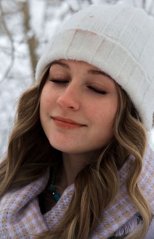 Smiling young woman with eyes closed wearing white knit hat and turquoise necklace in snowy outdoors.