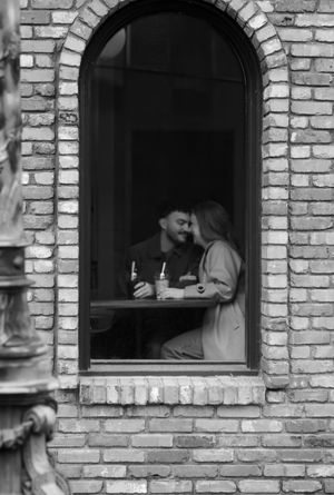 Black and white photo of a couple sharing an intimate moment at a cafe window.