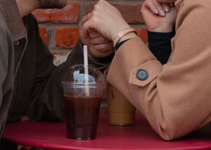 Couple sharing an iced coffee drink with a straw at a red café table outdoors.