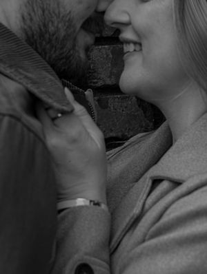 Black and white close-up of smiling couple almost kissing against a brick wall background.