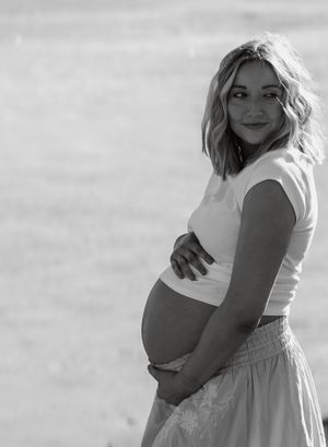 Black and white maternity portrait of pregnant woman cradling her baby bump outdoors.