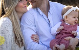 Young family with mother, father, and baby girl in pink romper posing outdoors together.
