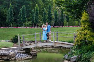 Couple standing on a wooden bridge over a pond in a lush green garden park setting.