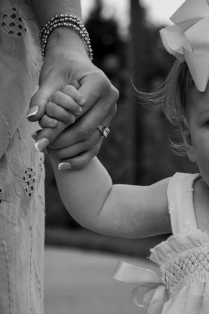 Black and white photo of a mother holding her young daughter's hand, both dressed elegantly, showcasing a tender moment.