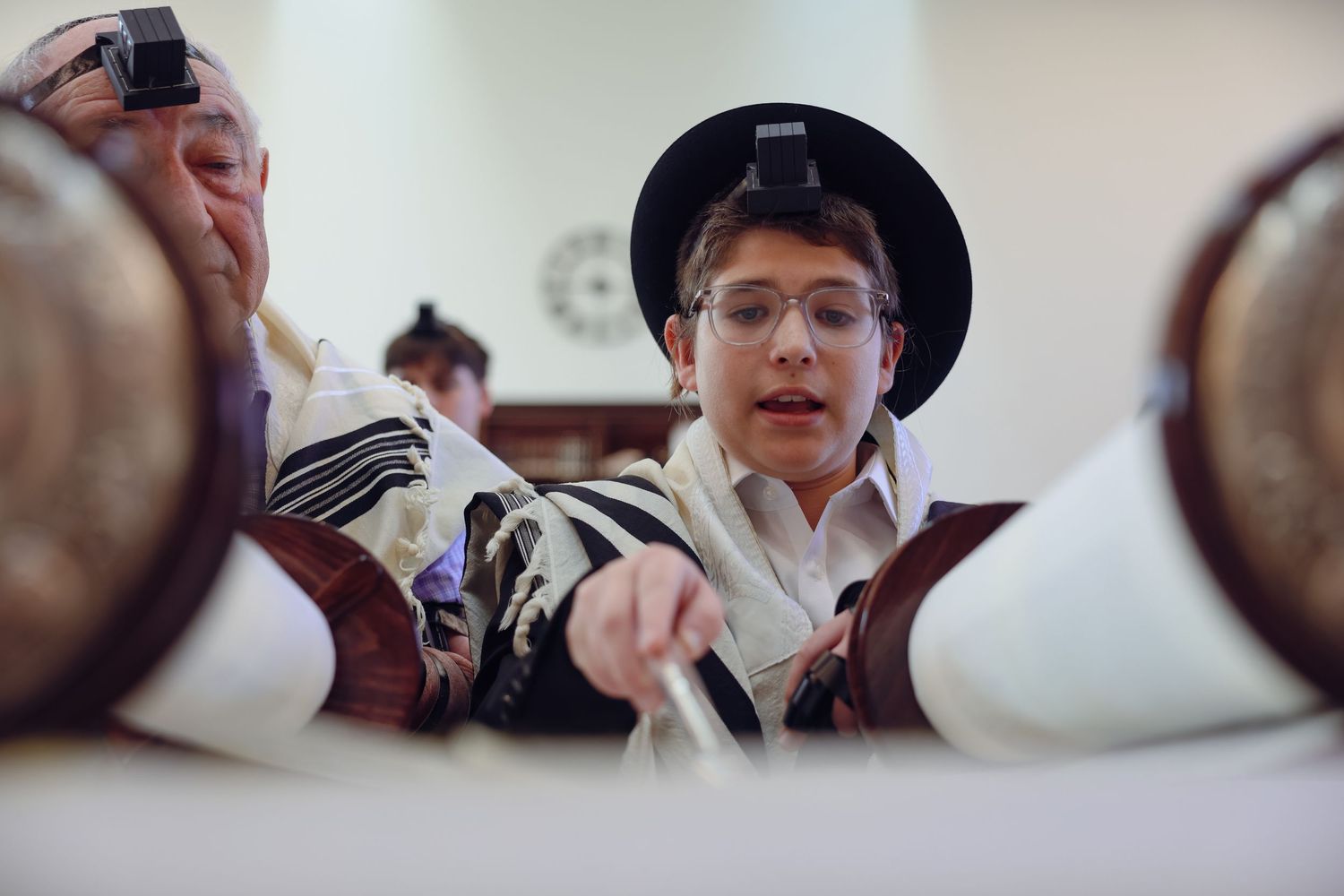 Young boy reading Torah scroll during Bar Mitzvah ceremony wearing tallit and tefillin.