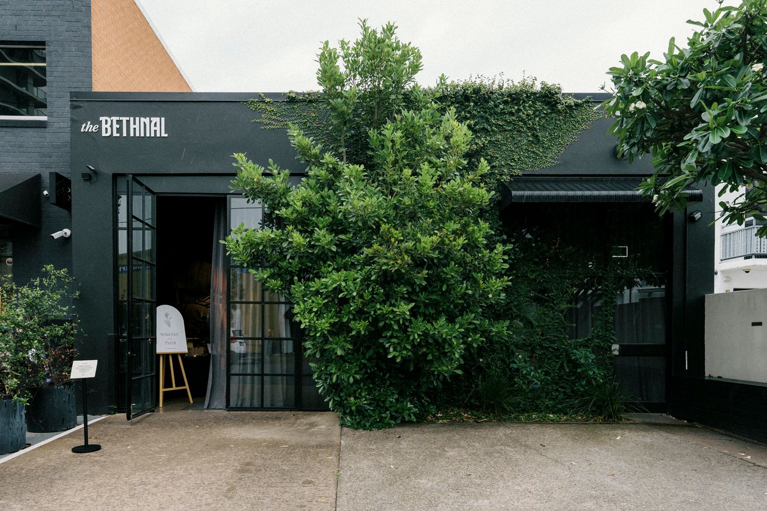 The Bethnal dark exterior with lush green foliage framing the entrance of a modern black building. the bethnal. Newstead Brisbane