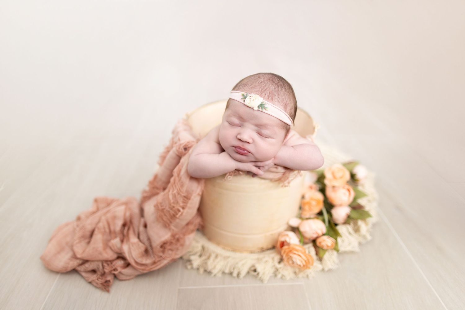Newborn baby sleeping peacefully in a wooden bucket with pink roses and a blush floral wrap.