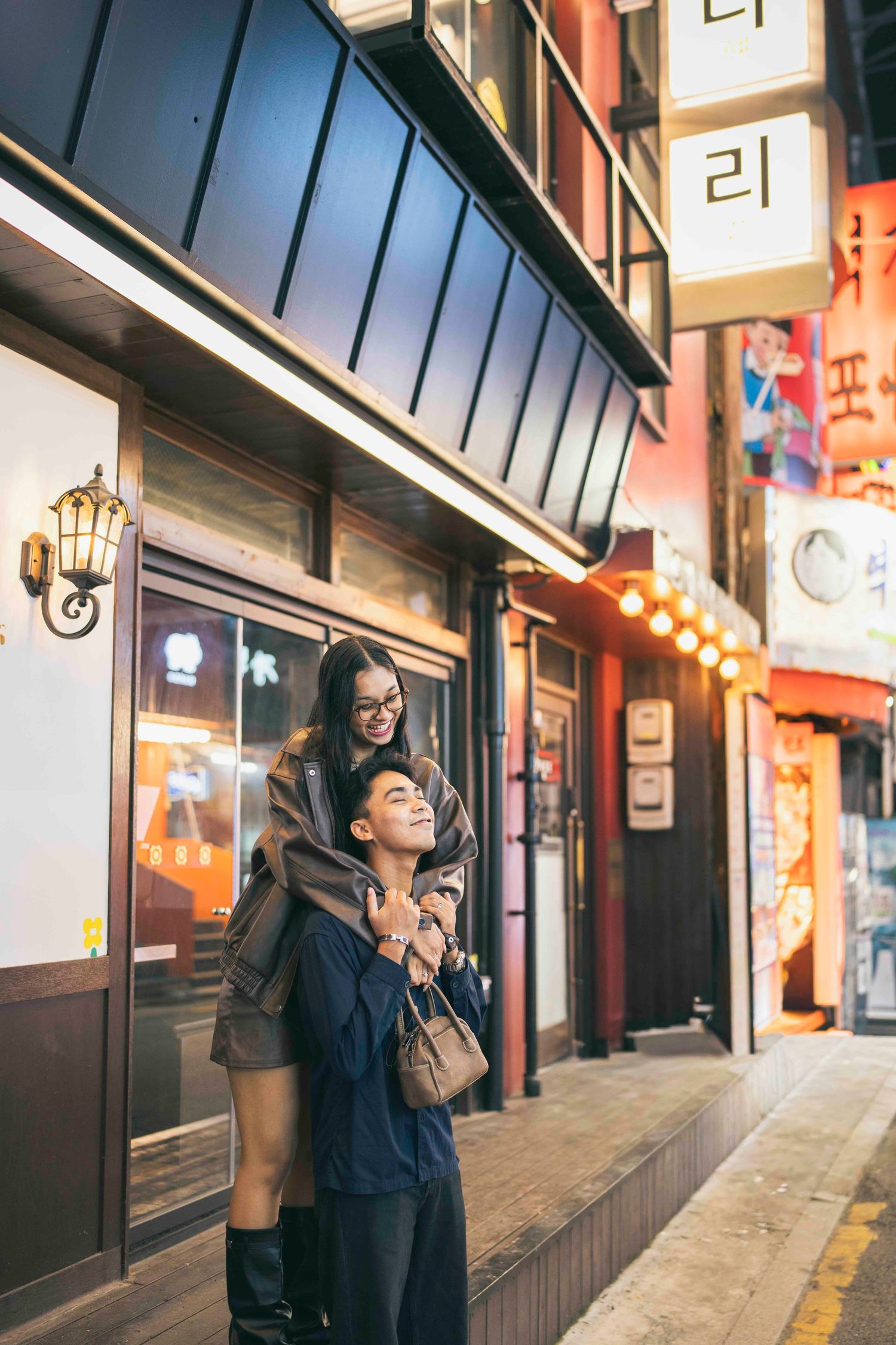 Couple embracing and laughing on a vibrant Korean street at night, surrounded by illuminated signs and storefronts.