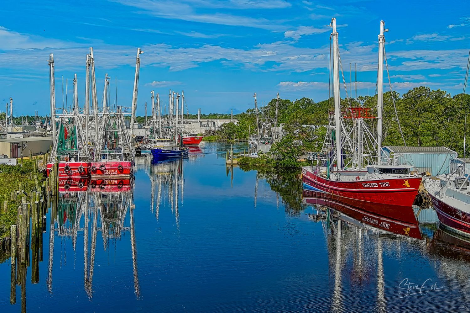 Colorful fishing boats docked along a quiet harbor, reflecting perfectly in calm blue waters. Fine art coastal photo by Steve Cole.