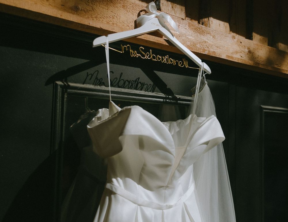 White strapless wedding dress hanging on personalized Mrs. Sebastiane hanger in rustic barn venue.