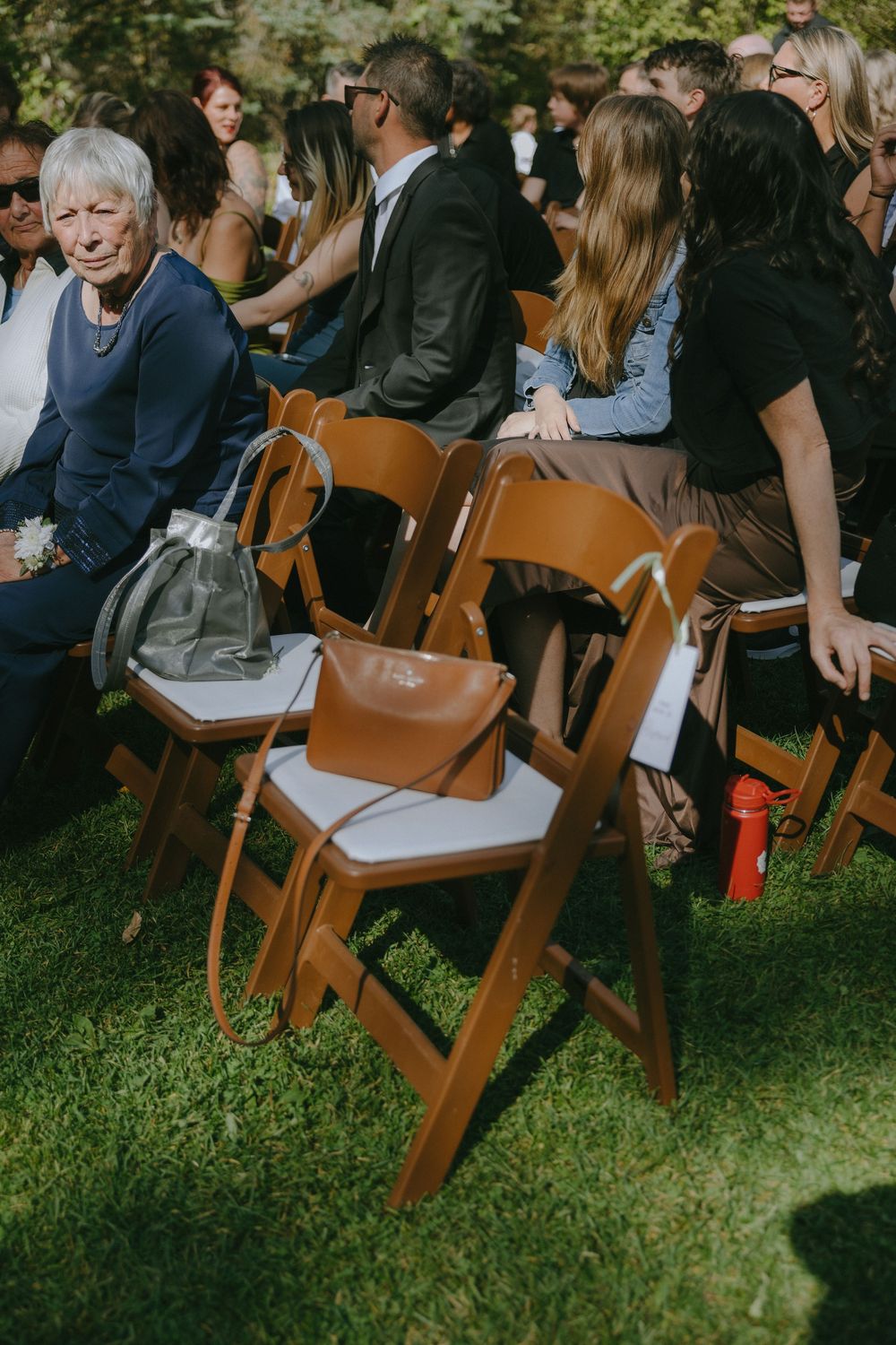 Wooden folding chairs with handbags at an outdoor wedding ceremony on green grass.