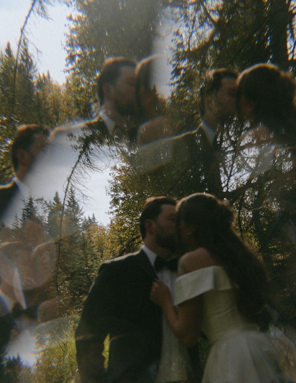 A couple shares a romantic kiss in a dreamy, lens-distorted forest wedding photo with soft light reflections.