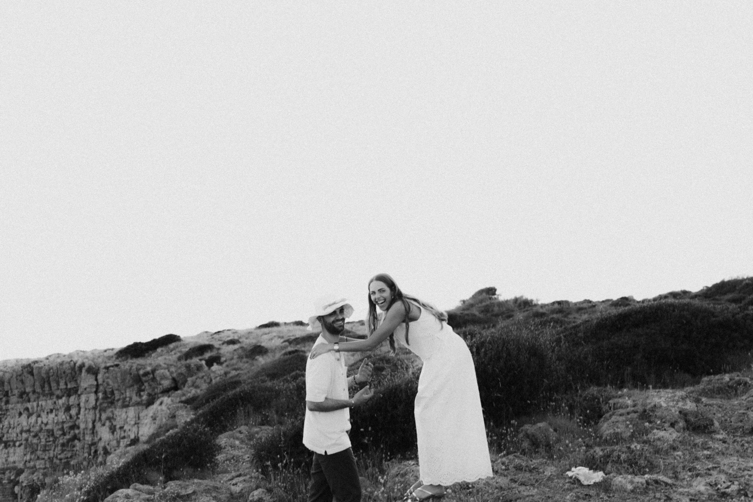 Black and white photo of a couple sharing a tender moment outdoors on a rocky hillside.