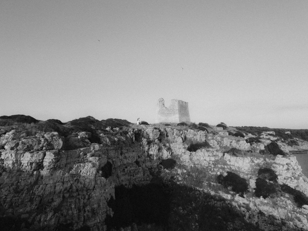 Black and white photo of ancient rocky coastline with historic stone tower ruins rising above rugged cliffs.