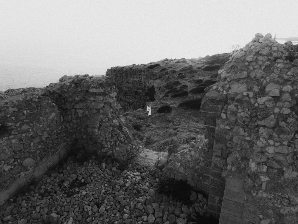 Black and white photo of ancient stone ruins on a rocky coastline with misty ocean in the background.