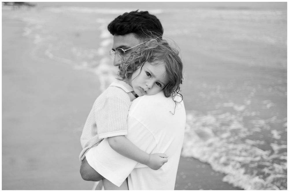 Father lifting his daughter beneath tropical leaves during a family session in Punta Mita. Black and White Beach Portraits