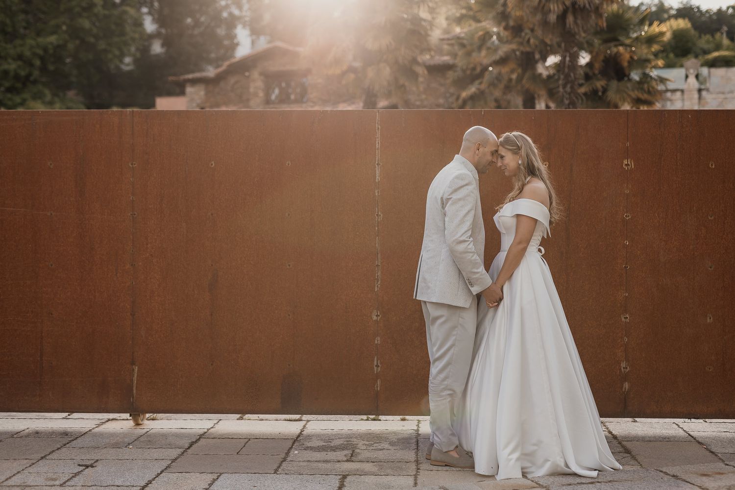 Bride and groom share a romantic moment in golden sunlight, standing close together against a rustic metal wall.