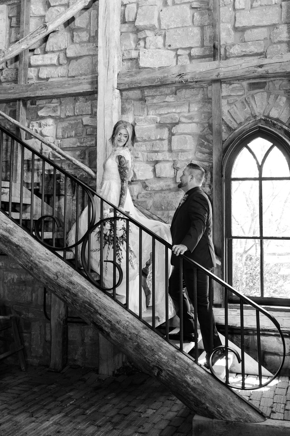 Black and white photo of bride and groom on ornate staircase in stone castle venue.