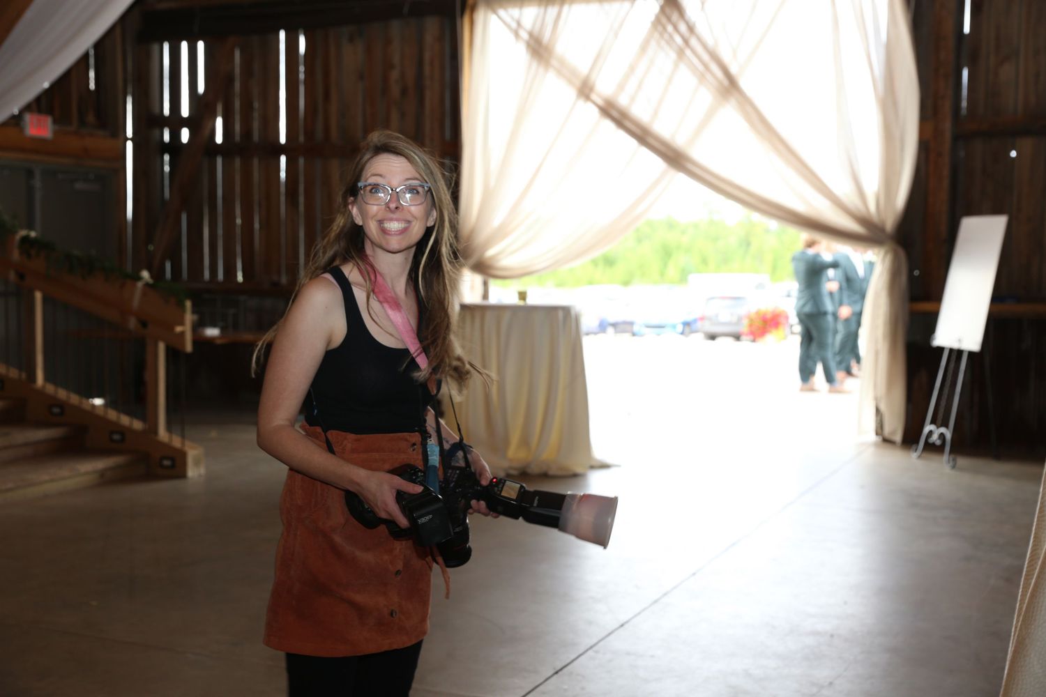 Female photographer holding a camera in a rustic barn venue decorated with draped curtains for an event.