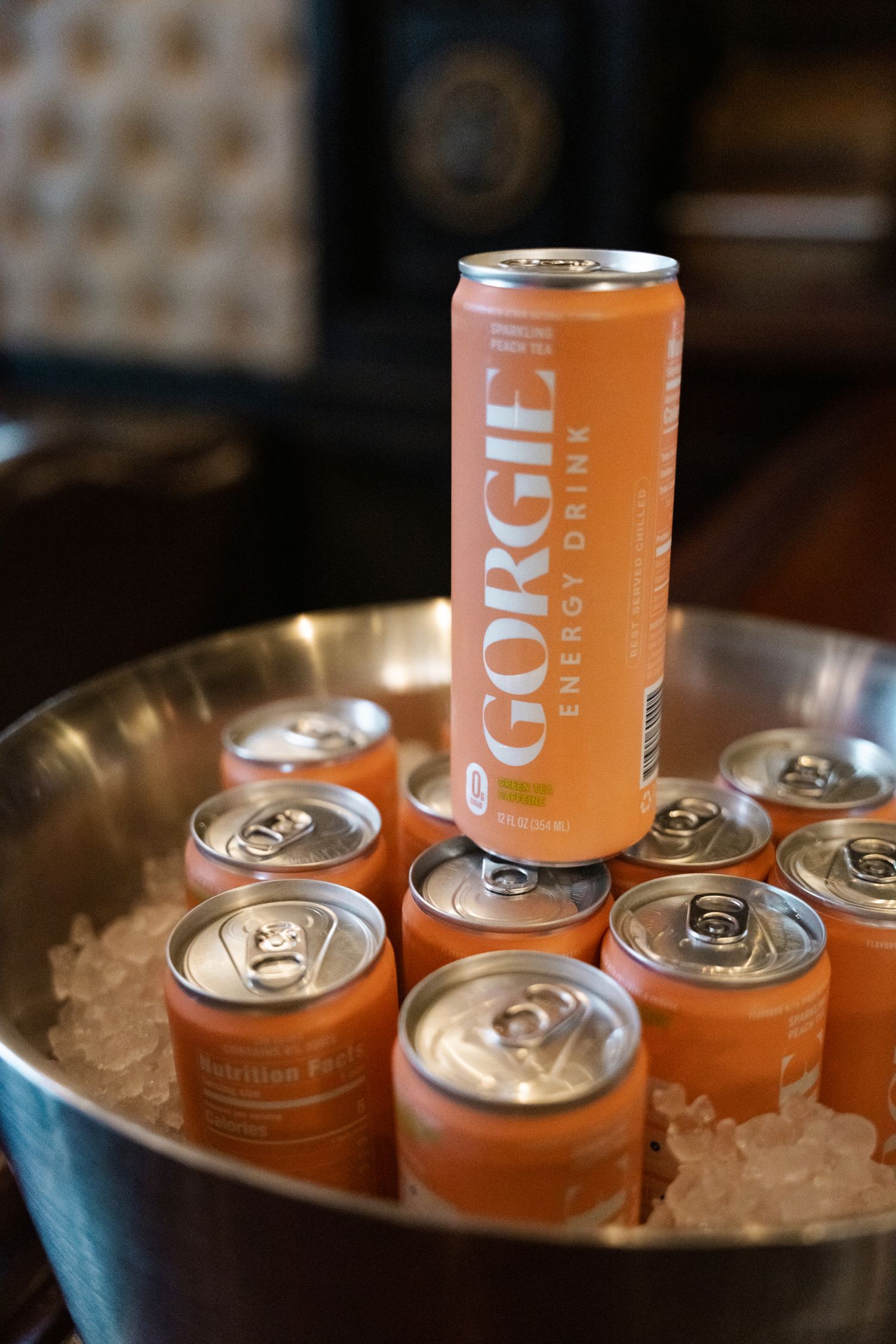 A tall orange Gorgie Energy Drink can displayed upright in an ice bucket surrounded by smaller orange cans.
