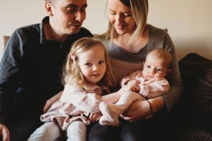 A family of four sits together on a couch for an intimate portrait session.