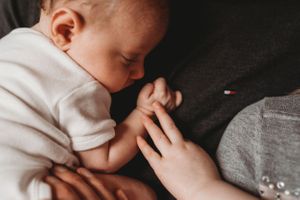Close-up shot of a baby's hand grasping another person's finger against a dark background.