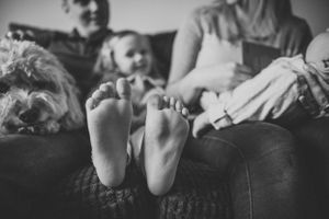 Black and white photo of small bare feet on a couch with family members visible in background.
