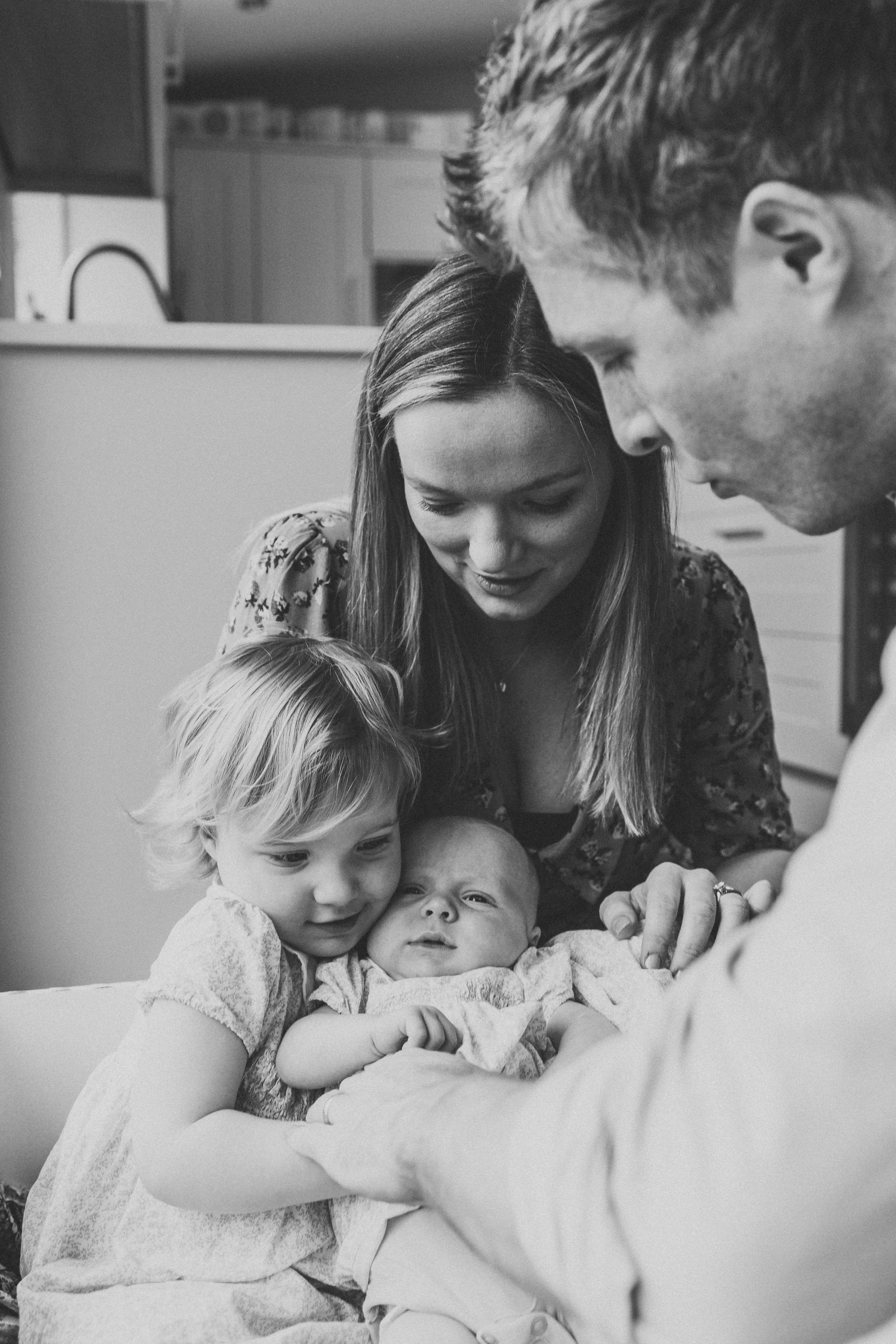 Family gathered around newborn baby in intimate black and white portrait.