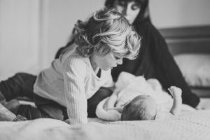 Black and white image of siblings bonding with newborn baby on bed.