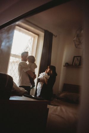Silhouetted family sharing intimate moment by window in dimly lit room.