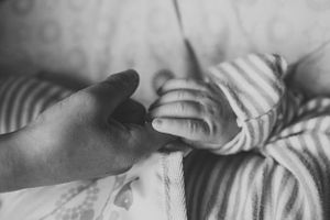 Black and white photo of adult and baby hands touching on white fabric.