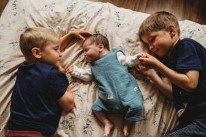 Three siblings lying together on floral bedding having peaceful moment.