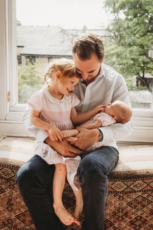 A touching family moment by a sunny window on a patterned rug.