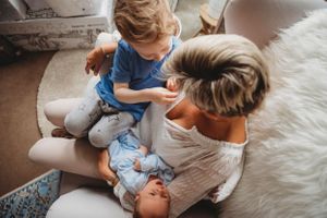Family members sit together on a plush white rug while bonding with their newborn.
