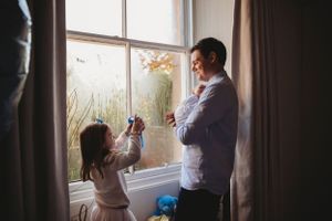 A heartwarming family moment by a sunlit window with fall foliage visible outside.
