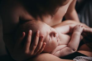 Gentle hands cradling sleeping newborn in intimate low-light setting.