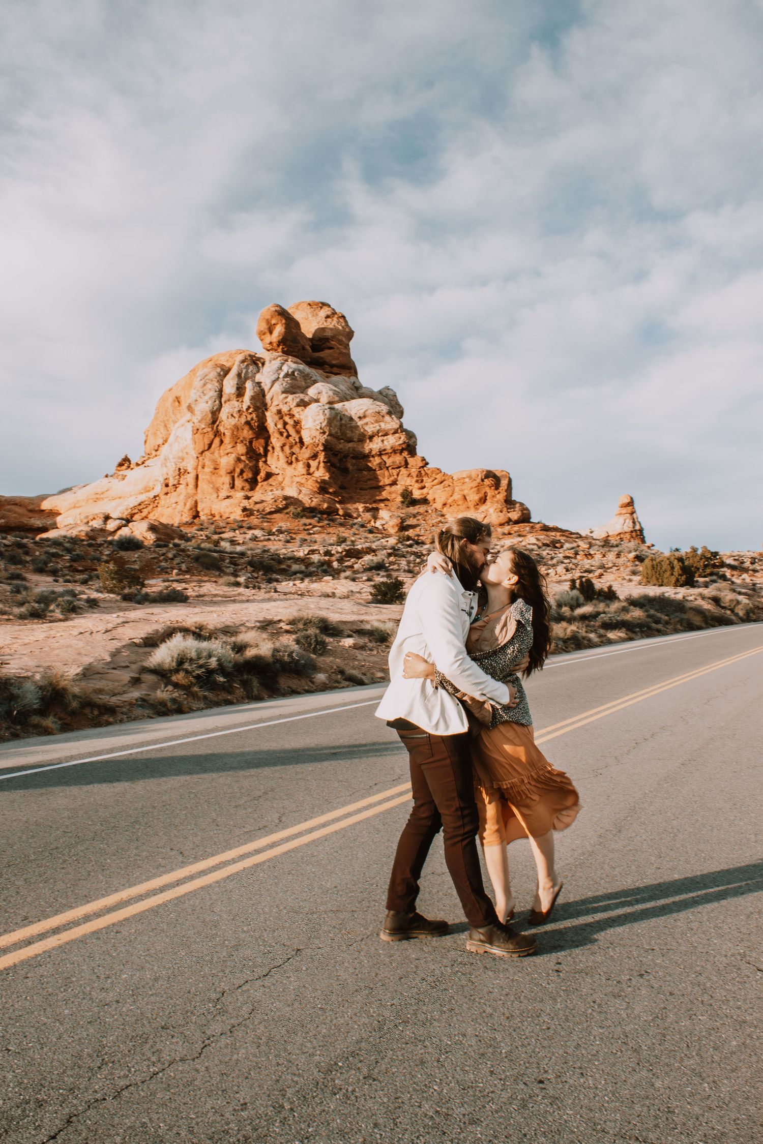 Couple embracing on desert road with red rock formations under blue sky in Southwest USA.