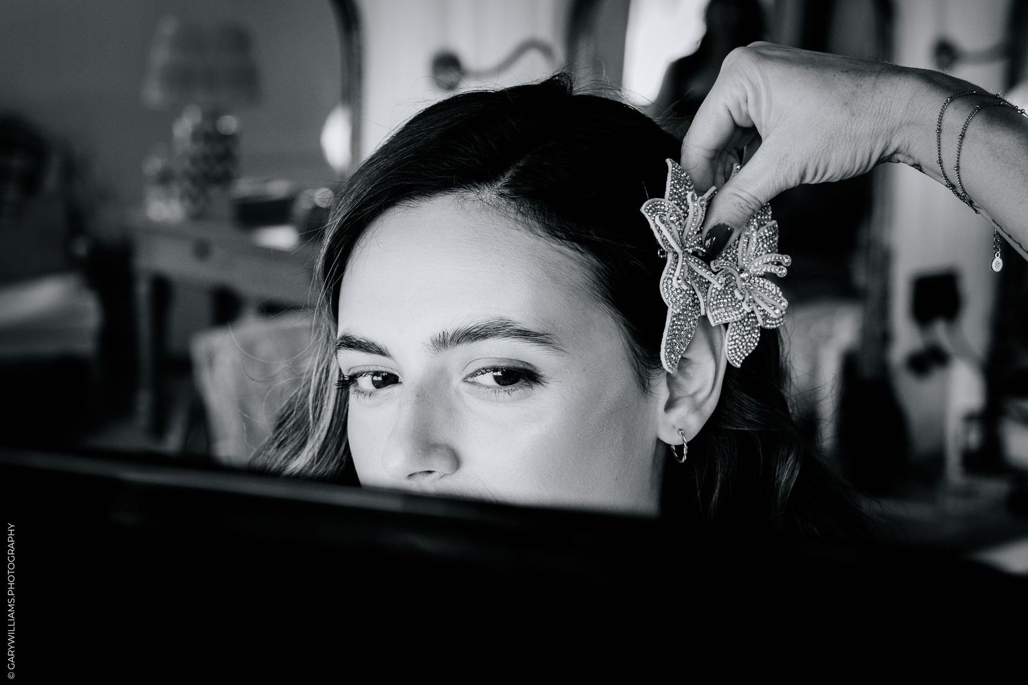 Black and white photo of a young woman having a floral hair accessory placed in her dark hair.