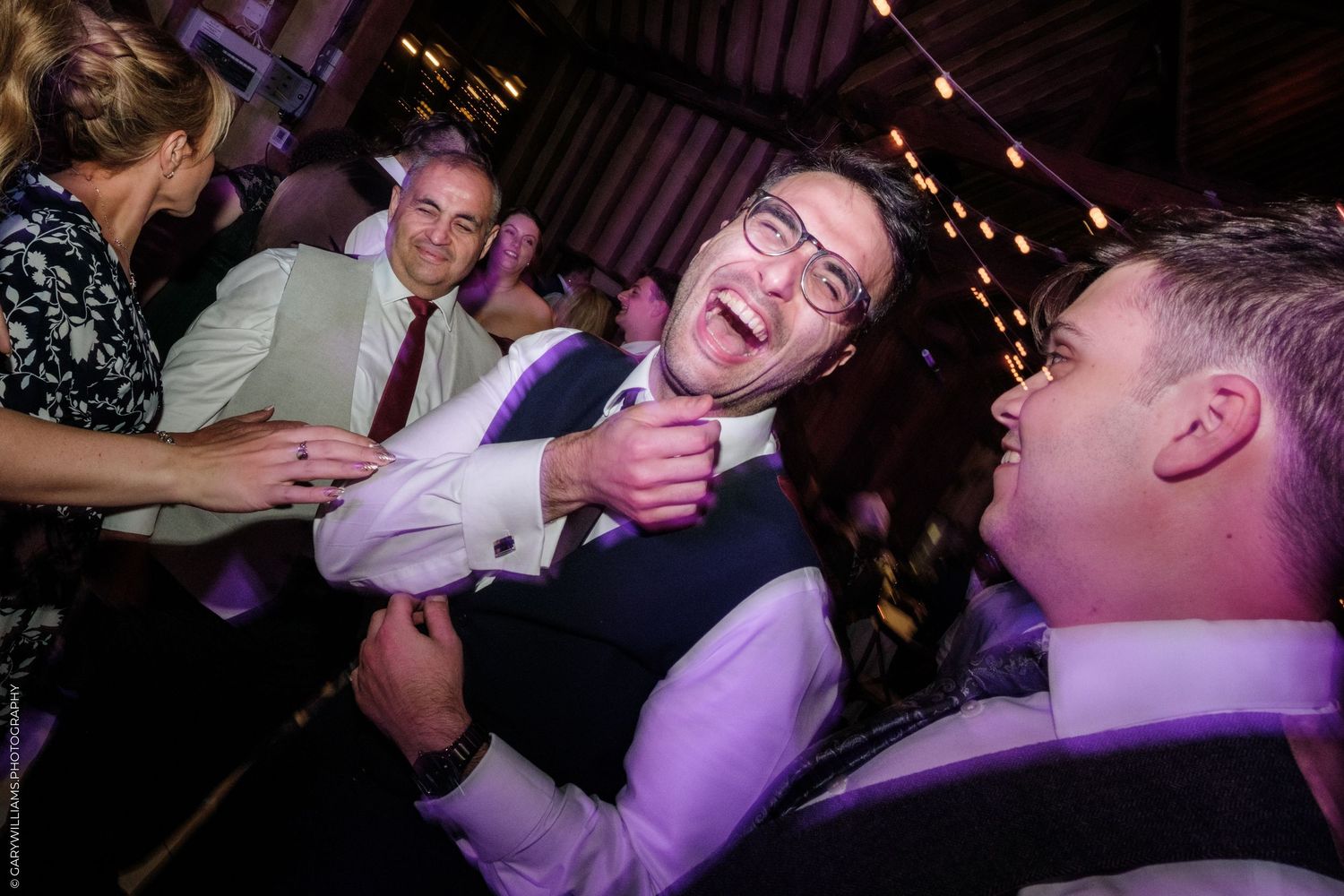 Men laughing and celebrating at a lively wedding reception party in a warmly lit venue.