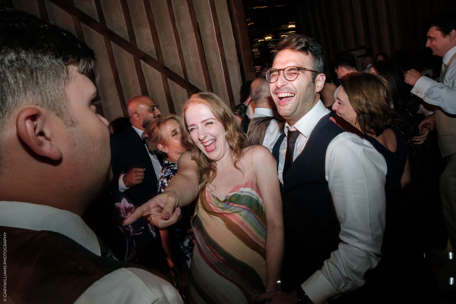 Guests laughing and dancing at a lively wedding reception party in a dimly lit venue.