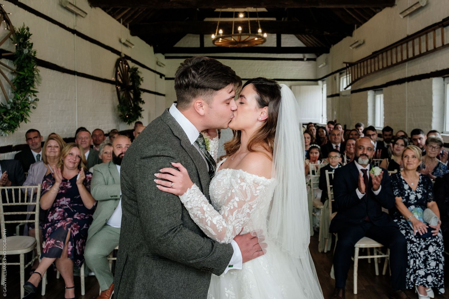Bride and groom share first kiss at wedding ceremony in elegant venue with seated guests.