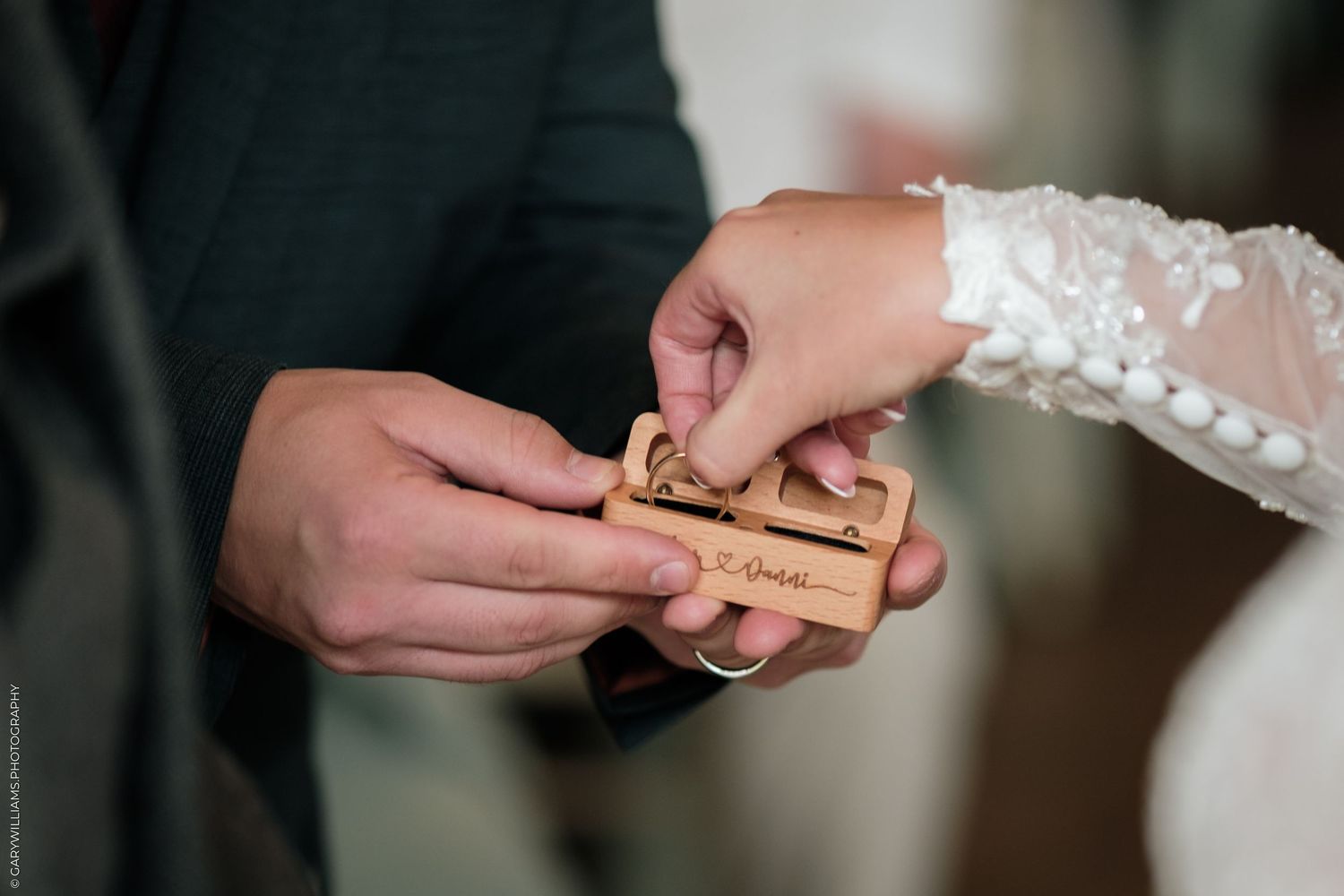 Bride and groom exchanging rings from a wooden ring box during wedding ceremony.