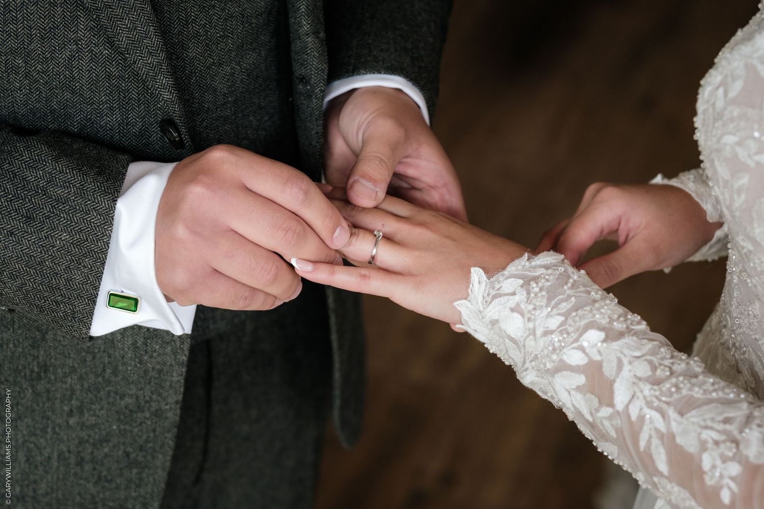 Groom placing a wedding ring on bride's finger during ceremony, bride wearing lace dress sleeve.